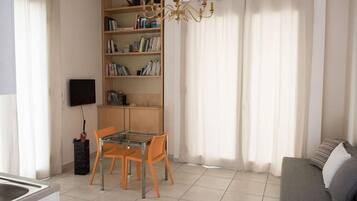 Ein Wohnzimmer mit einer Couch, einem Esstisch mit Stühlen, einem Bücherregal und einem Fernseher.