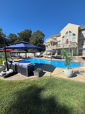 A swimming pool with lounge chairs and umbrellas, surrounded by a well-maintained lawn and a large house with a balcony. - Fully Furnished 2BR Apartment, Pool Access & All Amenities/Utilities Included (Fort Washington)