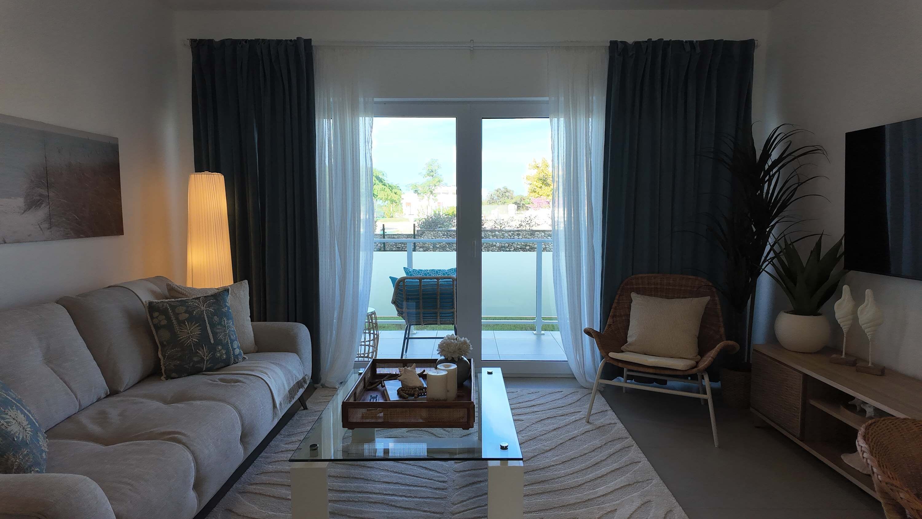 Una sala de estar con sofá, sillón, mesa de centro y vistas al exterior a través de un ventanal.