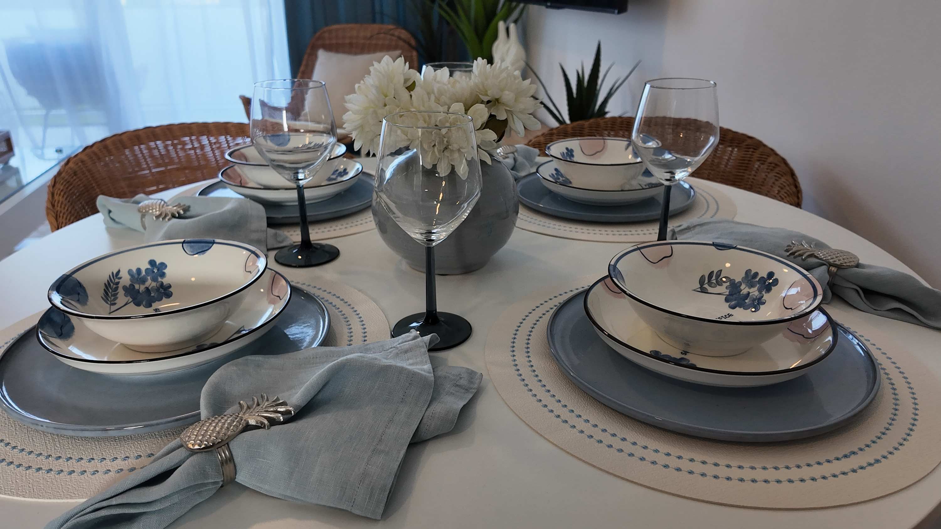 A table set with white and blue patterned bowls, clear glassware, and a vase with white flowers.