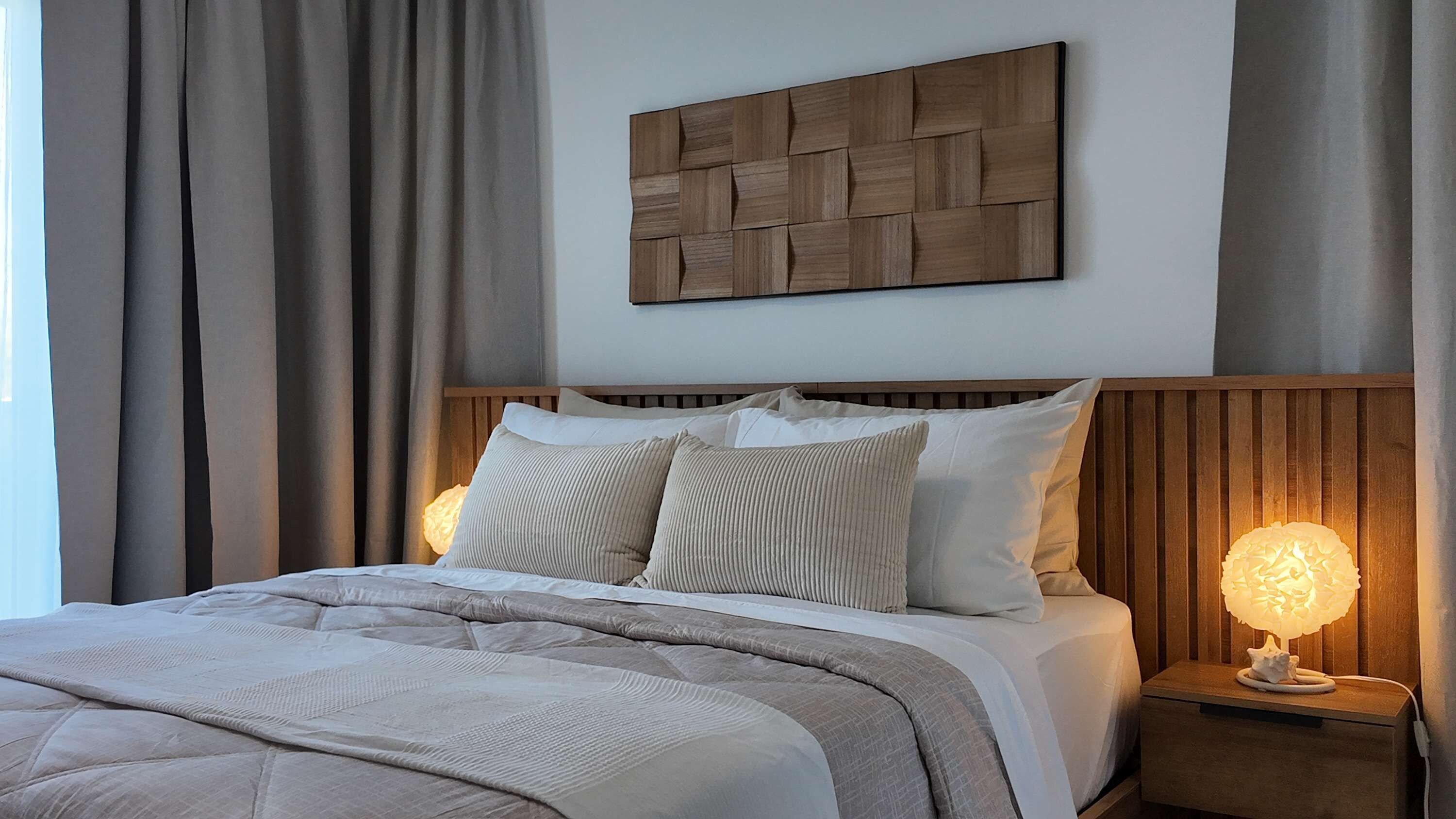 Un lit bien fait, avec une tête de lit en bois, une lampe de chevet et une œuvre d’art accrochée au mur.