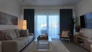 Ein Wohnzimmer mit einer Couch, einem Sessel, einem Couchtisch und einem an der Wand befestigten Fernseher.