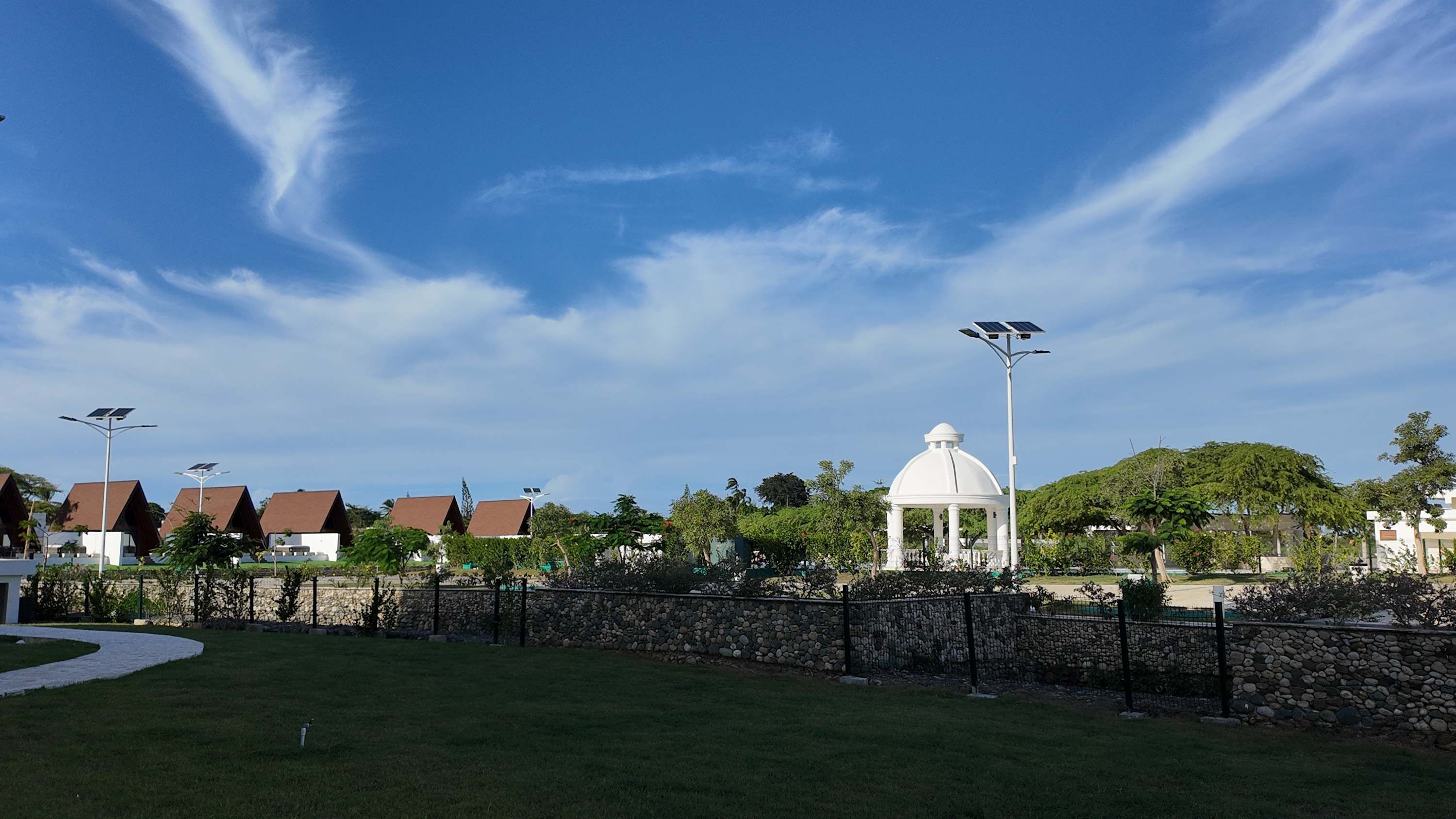 Un parque con un quiosco blanco, farolas solares y casas al fondo.