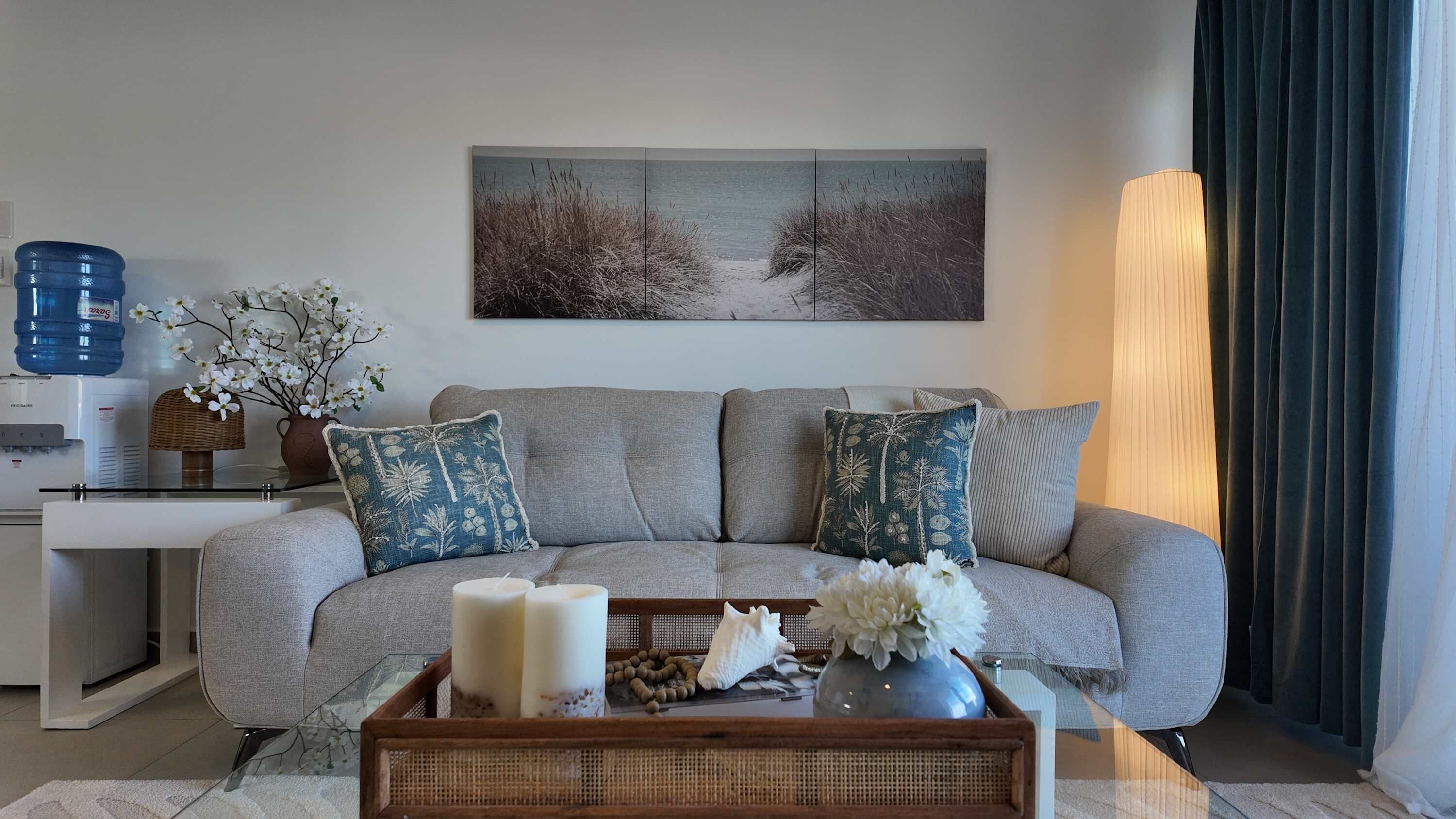 Una sala moderna con un sofá gris, almohadones decorativos, una bandeja con velas y una obra de arte colgada en la pared.