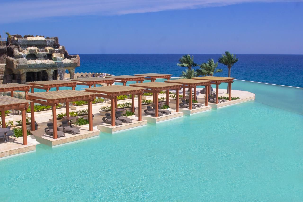 A resort pool area with lounge chairs and umbrellas, overlooking the ocean.