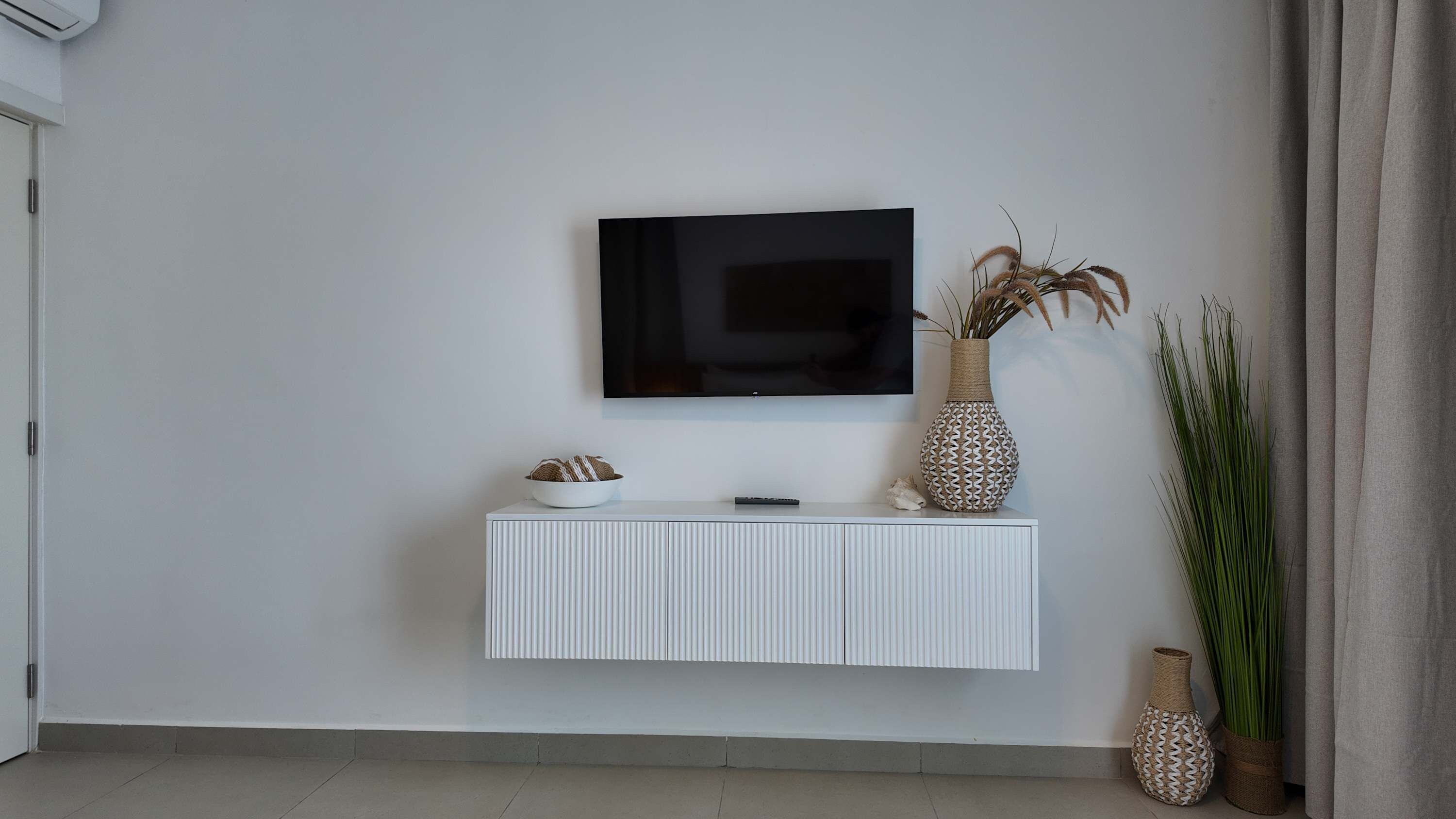A modern living room with a mounted TV, a white console table, and decorative vases.