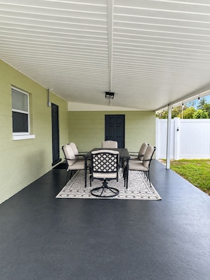 A covered patio area with a table and chairs, a door, and a white fence. - Boho Nest - Near Busch Gardens & USF (Tampa)
