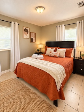A bedroom with a bed, nightstands, a lamp, a rug, and curtains. - Boho Nest - Near Busch Gardens & USF (Tampa)
