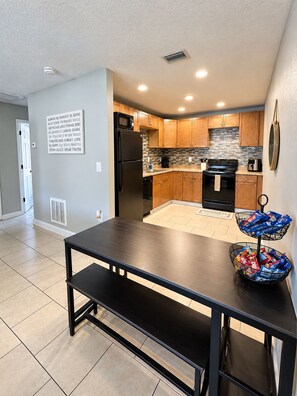 A modern kitchen with wooden cabinets, a black refrigerator, and a tiled backsplash. - Boho Nest - Near Busch Gardens & USF (Tampa)