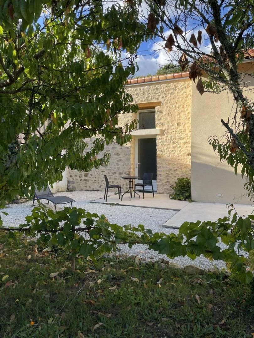 Un bâtiment en pierre avec une porte, une terrasse avec des chaises et un jardin.