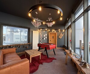 Ein gemütliches Zimmer mit Fußballtisch, Ledersofa und rotem Teppich.