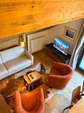 Ein gemütliches Wohnzimmer mit einer Couch, zwei Sesseln, einem Couchtisch, einem Fernseher und einem Kamin.