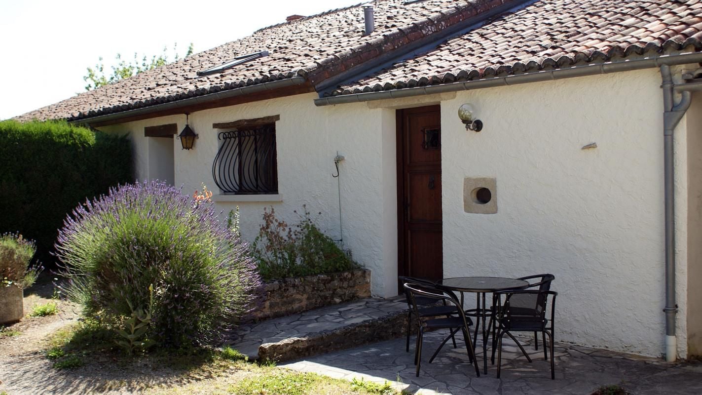 A building with a tiled roof, a door, and a small outdoor seating area with chairs.