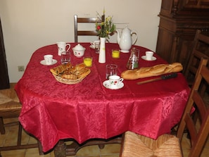 A dining table set with a red tablecloth, various cups, a teapot, a pitcher, a basket of bread, and a loaf of bread. - La Boulitte - ASNOIS (ASNOIS)