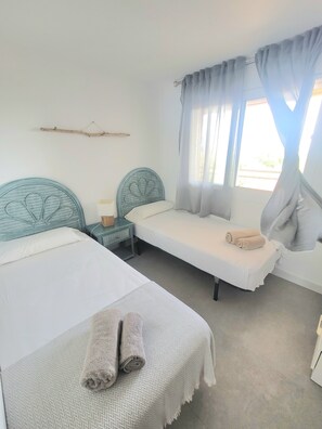 A room with two beds, a bedside table with a lamp, a window with curtains, and a wall-mounted branch decoration. - Beautiful, relaxing apartment with views in Sagaró (Sant Feliu de Guíxols)