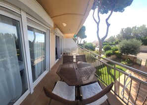 Un balcon avec une table et des chaises, une porte-fenêtre coulissante et une vue sur la verdure environnante et la rue.