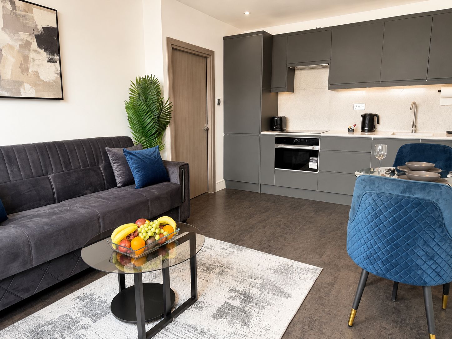 Ein modernes Wohnzimmer mit einer Couch, einem Glastisch mit Obst und einem blauen Sessel.
