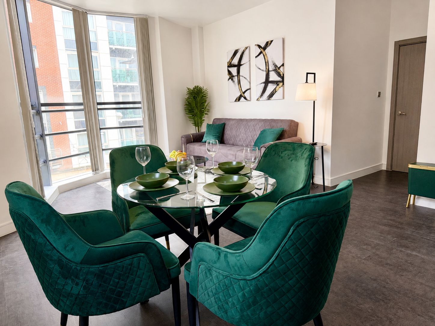 A dining area with a round table, green chairs, and a sofa in the background.
