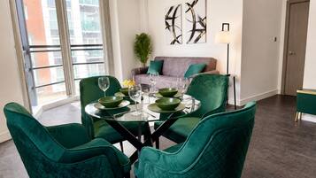 A dining area with a round table, green chairs, and a sofa in the background.