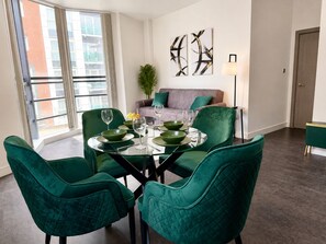 A dining area with a round table, green chairs, and a sofa in the background. - Modern 2 Bedroom Serviced Apartment West Street Sheffield (Sheffield)