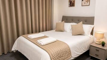 A neatly made bed with a beige quilt, two pillows, and two folded towels.