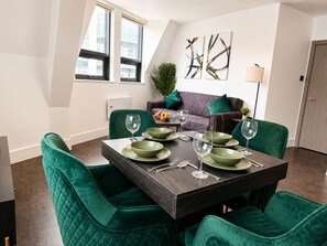 A dining area with a dark wooden table, green upholstered chairs, and a modern aesthetic. - Modern 2 Bedroom Serviced Apartment West Street Sheffield (Sheffield)