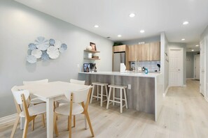 Een moderne keuken met een centraal eiland, witte barstoelen en een eettafel met stoelen.