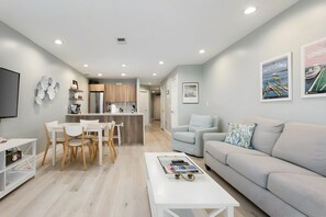 A modern living room with a grey sofa, a coffee table, and a dining area with white chairs. - Tidal Retreat 217 | Balcony | Direct Beach Access | Near Downtown & TART Trail (Traverse City)