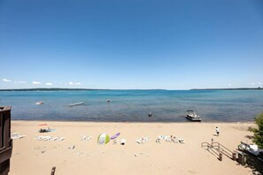 A beach with lounge chairs, a tent, and a boat in the water. - Tidal Retreat 217 | Balcony | Direct Beach Access | Near Downtown & TART Trail (Traverse City)