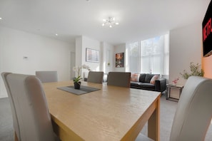 A modern living room with a wooden dining table, two sofas, and a TV mounted on the wall. - Modern 5 Bed Flat in Thornaby Road For Big Groups (Thornaby)