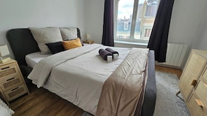 Ein Hotelzimmer mit Bett, Nachttisch, Lampe und Blick auf die Stadt durch ein Fenster.