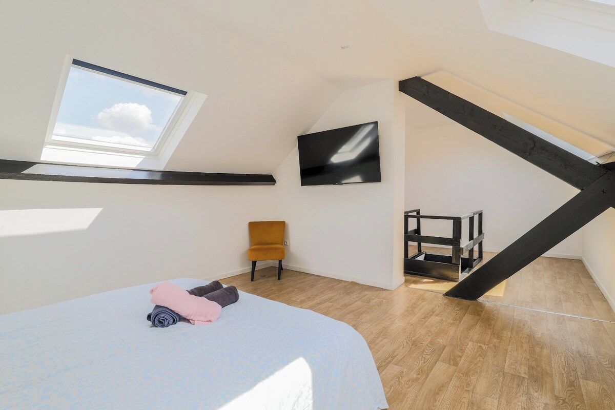Een slaapkamer met een dakraam, een bed met opgerolde dekens, een televisie en een houten stoel.