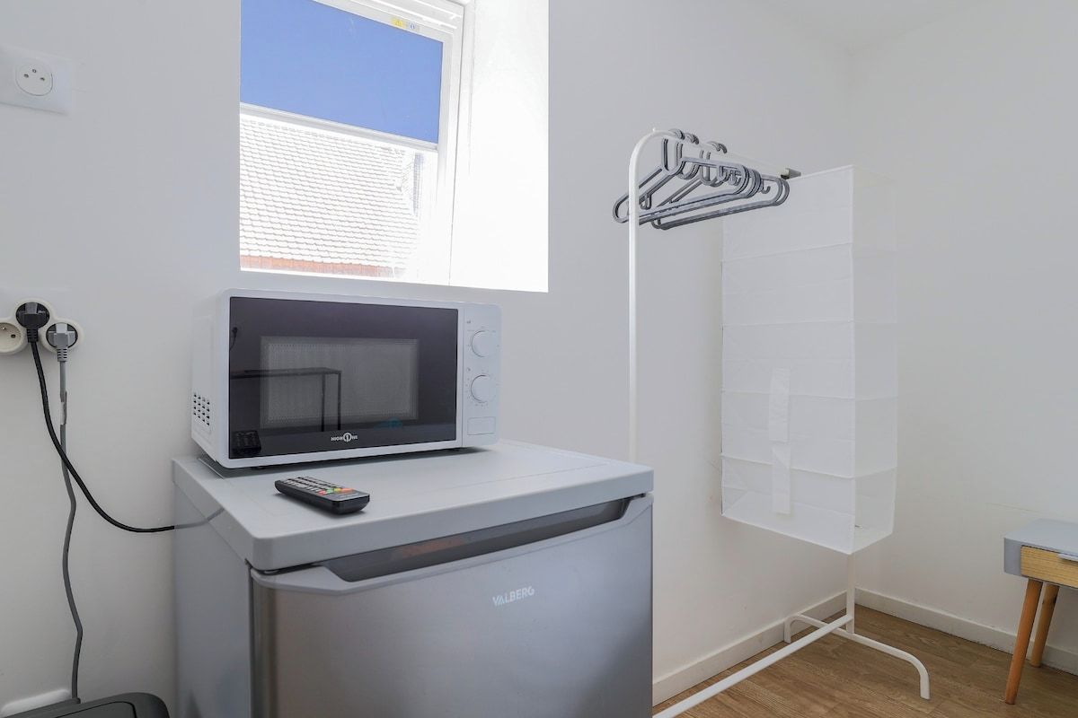 A compact kitchenette with a microwave, a small refrigerator, and a window with a view of a building.