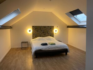 A bedroom with a sloped ceiling, skylights, a bed with a patterned headboard, bedside lamps, and a small bedside table. - Le Nid Cosy 4, Balnéo 2 lits wifi (Tourcoing)