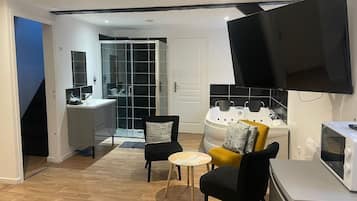 A modern living room with a flat-screen TV, a sofa, a coffee table, and a kitchen area with a microwave.