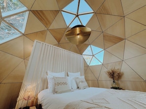 A bedroom with a geometric wooden ceiling, a bed with white bedding, and a hanging light fixture. - Logement insolite, Dôme bois piscine-Coeur Cristal (Luxembourg)