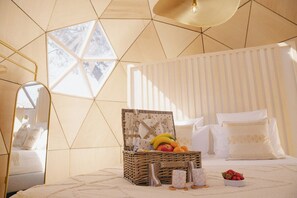 Ein Schlafzimmer mit einem geometrischen Deckendesign, einem Korbfruchtkorb, einem Nachttisch mit einer Tasse und einem Bett mit weißer Bettwäsche.