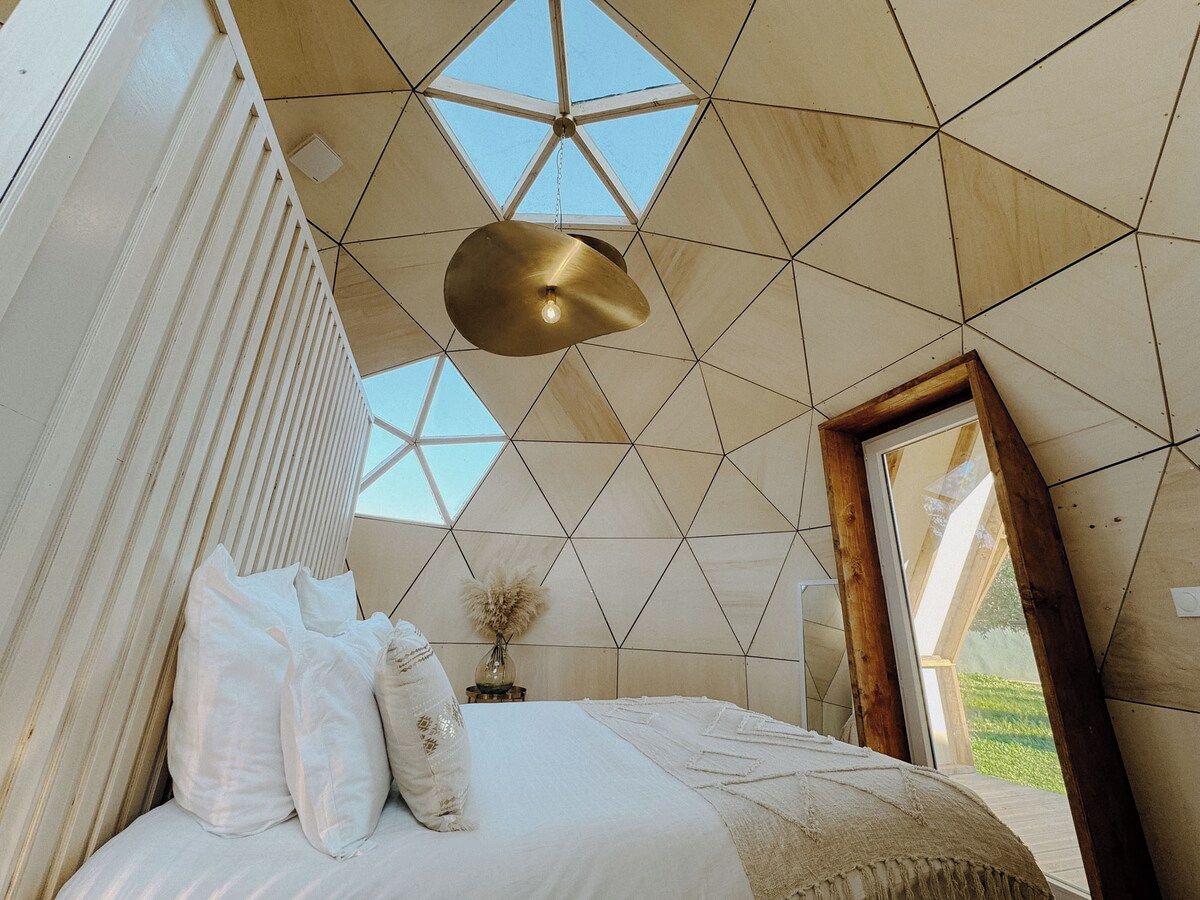 Un dormitorio con un diseño geométrico en el techo, una cama con ropa de cama blanca y una lámpara colgante.