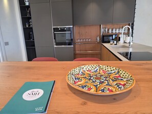 A modern kitchen with a wooden table, a decorative plate, and a green book titled 'SMIL'. - MiCasa Jacuzzi & Rooftop SicilyMyHome (Noto)