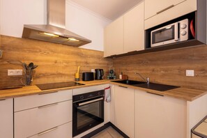 A compact kitchen with a built-in microwave, oven, and sink, featuring wooden accents and modern cabinetry. - Rated apartment with pool & quiet terrace (Valras-Plage)