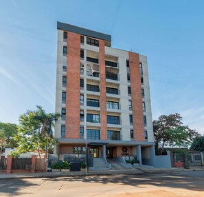 A multi-story residential building with a flat roof, large windows, and a central entrance with a staircase. - Modern Two-Bedroom in Luque with Pool&Gym Access (Luque)