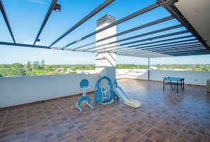 A spacious outdoor area with a wooden floor, a children's playset, and a table with chairs. - Modern Two-Bedroom in Luque with Pool&Gym Access (Luque)