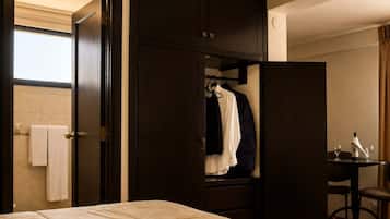 A hotel room with a bed, a wardrobe, a mirror, a small table with a bottle and glasses, and a towel rack.