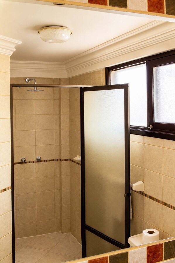 A bathroom with a shower enclosure, a toilet, and a window. - Calacoto King Suite | Garden + Concierge (La Paz)