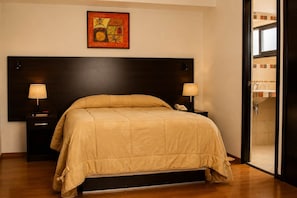 A hotel room with a large bed, bedside lamps, a telephone, and a painting on the wall.