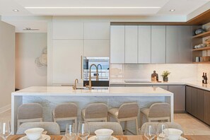 A modern kitchen with a central island, bar stools, and a dining table set for four. - Oceanfront Three-bedroom Condo with Infinity Pool (Nassau)