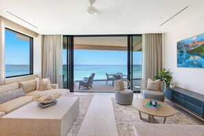 A modern living room with a large window overlooking the ocean, a sofa, a coffee table, and a dining area with chairs. - Oceanfront Three-bedroom Condo with Infinity Pool (Nassau)