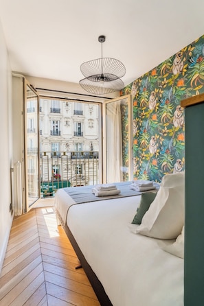 A bedroom with a bed, a view of a building through a glass door, and a patterned wall. - The Collection - Stylish 3BD next to Invalides! (Paris)