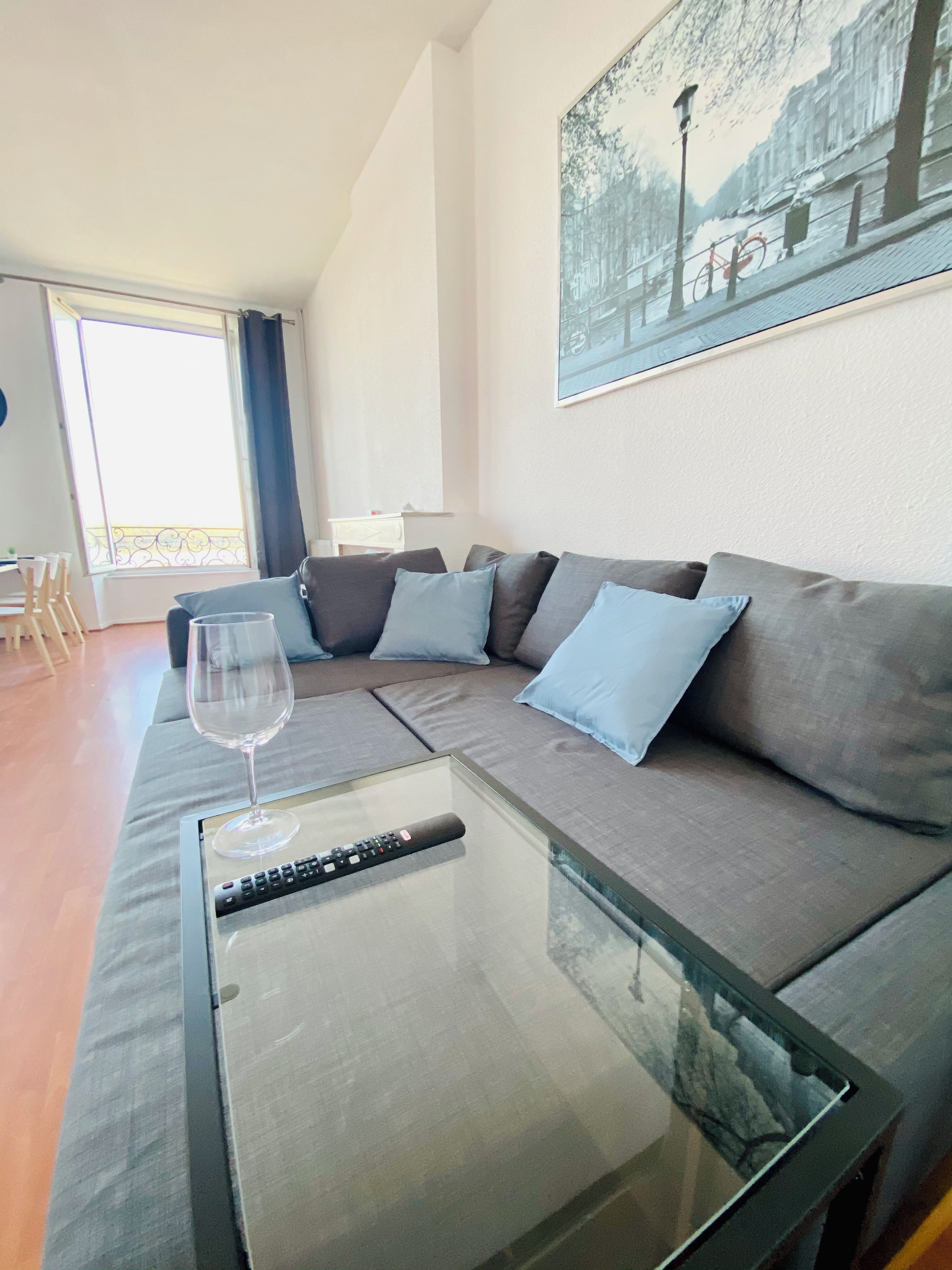 A modern living room with a glass coffee table, a remote control, and a wine glass.