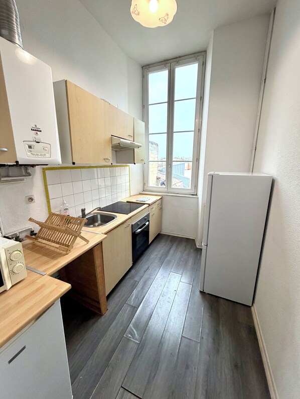 Een compacte keuken met een raam, een ingebouwde oven en een witte koelkast.